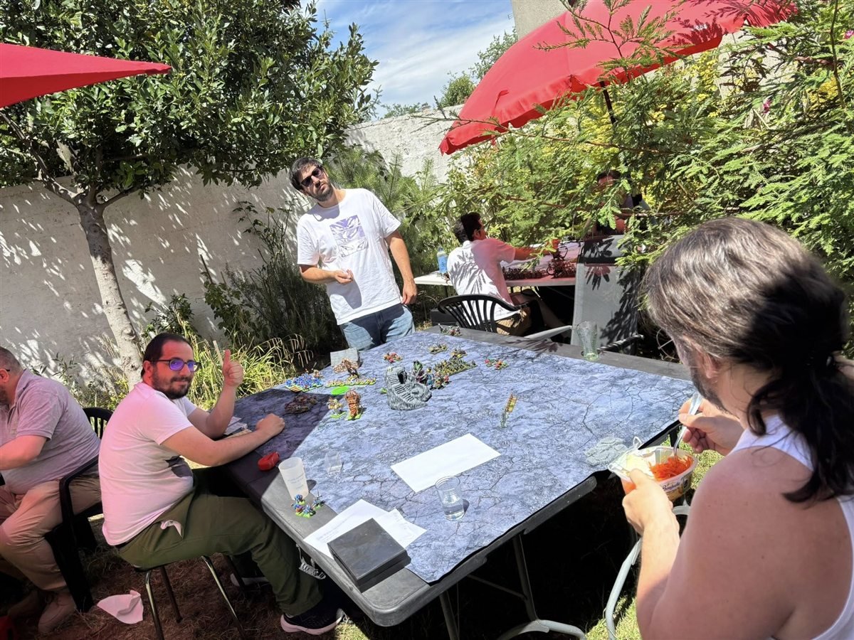 Joueurs reunis autour de tables de wargame dans un jardin